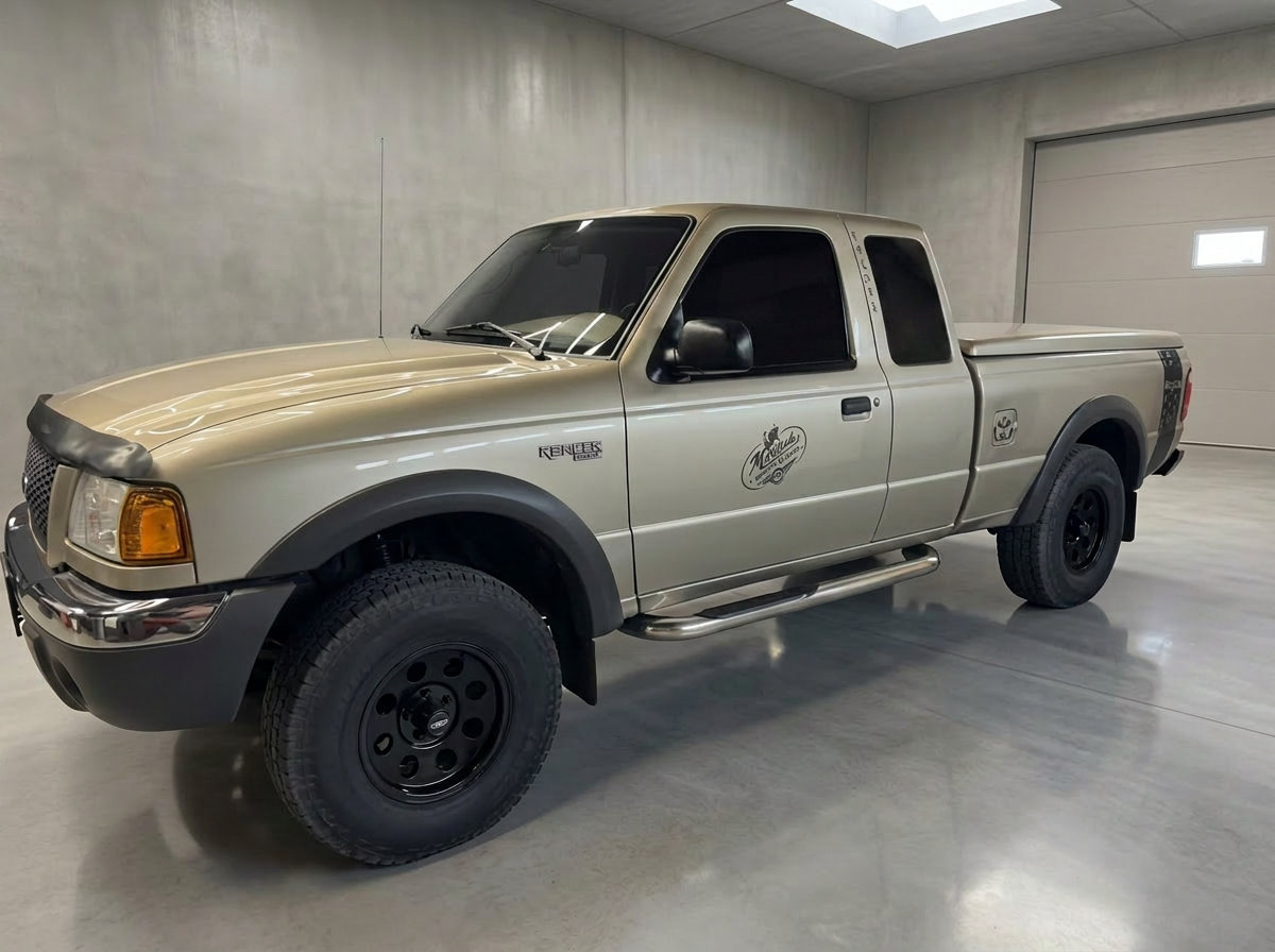 Metallic gold 2001 Ford Ranger XLT 4x4 with black rims and 31-inch mud tires in a minimalist concrete workshop